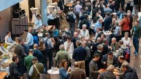 A large number of people gather in the foyer and engage in lively discussions while having a welcome coffee.